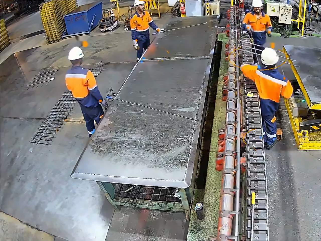 Camera view of workers in high-visibility clothing on a factory floor.