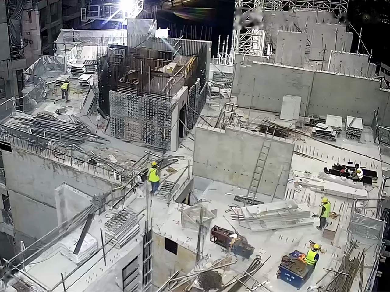 Camera view over a building under construction, with workers on an upper floor.