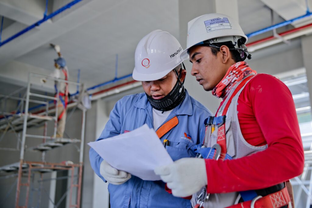 Two White Hat Construction Workers Discussing with a white paper in their hands